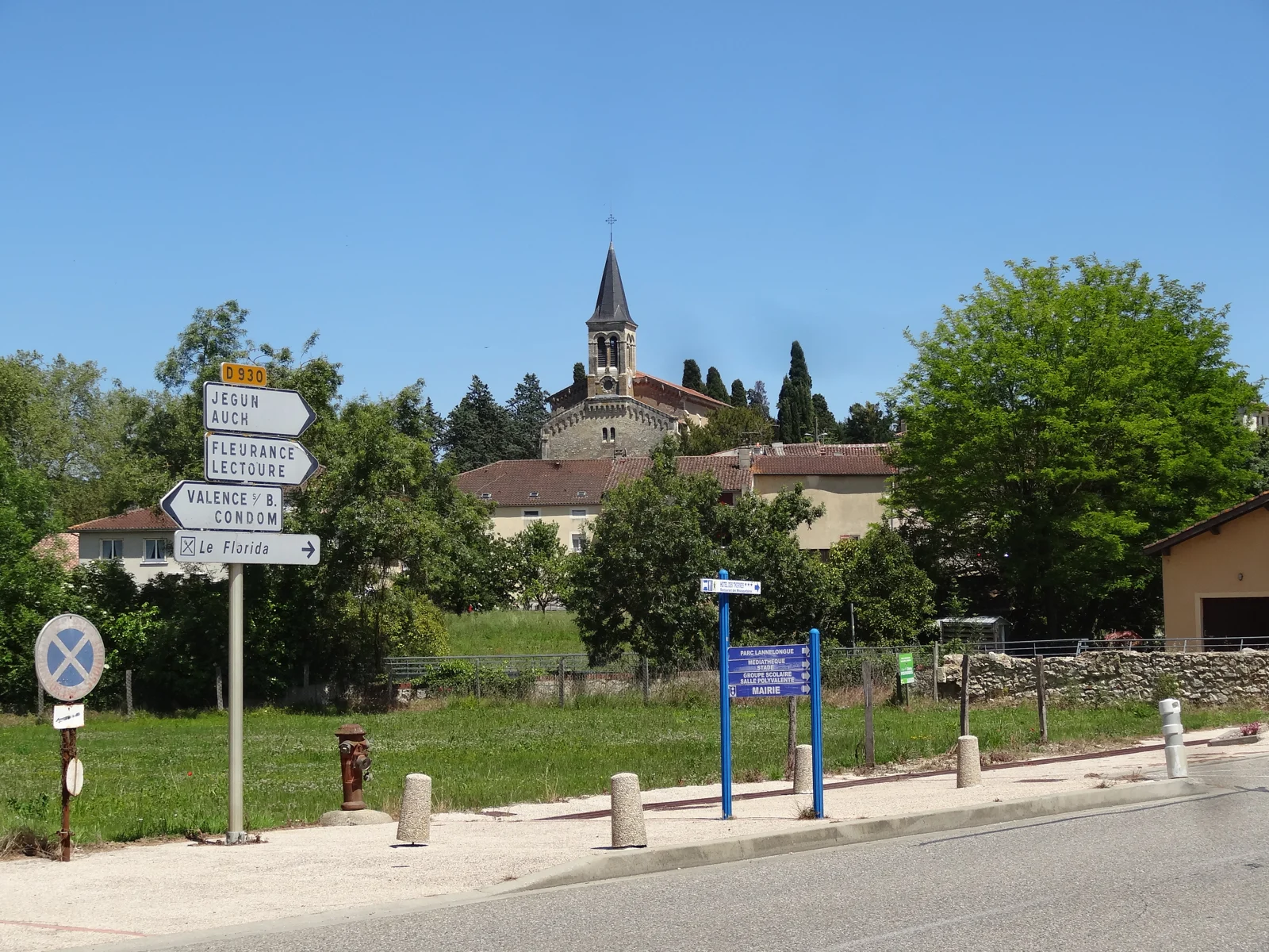 Le clocher de l’église dominant les toits de Castéra-Verduzan, derrière un carrefour et ses panneaux de direction