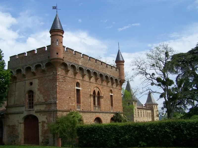 Bâtiment de brique à créneaux et tourelles de la partie du XVe siècle du château de Caumont, avec le logis en arrière-plan